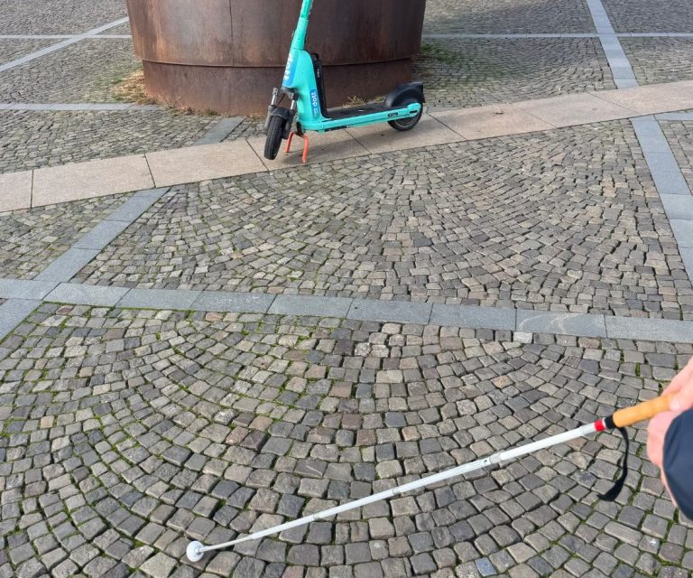 Typical obstacles for a blind or visually impaired person in public spaces. While crossing a square, artworks and a scooter block the path and make it harder to reach the destination.